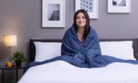 Woman seated in bed with Classic Weighted Blanket hugged around her shoulders